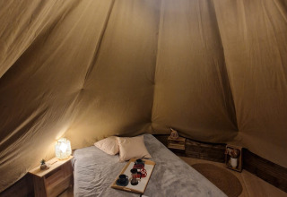 Knus interieur van een tipi tent met bed en zachte verlichting bij Tipi Junior, Weekend Glamping Resort, Italië.