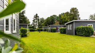 Spacious grassy yard with modern Group Yard Chalets, green hedges, and trees on a cloudy outdoor day.