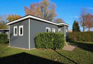 A modern Group Yard Chalet at De Scherpenhof in the Netherlands, surrounded by greenery and blue sky.