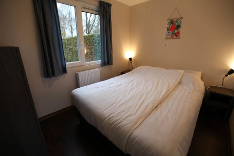 Soveværelse på Group Yard Chalets i De Scherpenhof, Holland med dobbeltseng og hyggelig belysning.