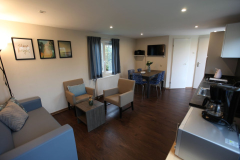 Modern living area in Group Yard Chalets at De Scherpenhof, Netherlands, featuring sofa, chairs, and kitchen.