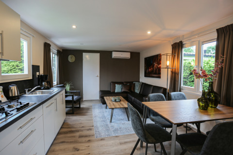 Moderne stue og køkken i Group Yard Chalets på De Scherpenhof, Holland, med spisebord og sofa.
