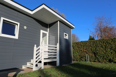 Indgangsparti til en moderne lodge på Group Yard Chalets, De Scherpenhof, med blå facade og hæk.