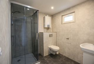 Moderne badeværelse med brusekabine, væghængt toilet og håndvask på Group Yard Chalets i Holland.