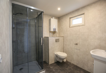 Modern bathroom with glass shower, wall-mounted toilet, and sink at Group Yard Chalets in the Netherlands.