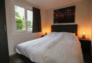 Cozy bedroom at Group Yard Chalets, De Scherpenhof, Netherlands, with double bed, window and artwork.