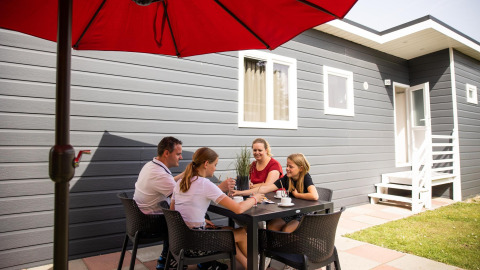 Family sitting outside under a red umbrella at a black table at Group Yard Chalets in De Scherpenhof, Netherlands.