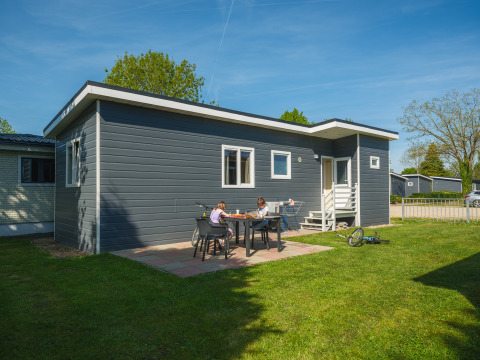To børn sidder ved et bord foran en moderne chalet ved Group Yard Chalets, De Scherpenhof, Holland.