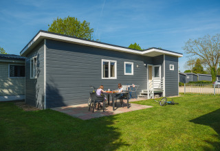 To børn sidder ved et bord foran en moderne chalet ved Group Yard Chalets, De Scherpenhof, Holland.