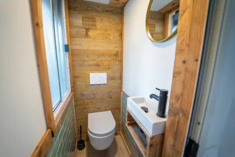 Moderne badkamer met houten wanden, hangend toilet, kleine wastafel en zwarte kraan bij Bohemian Lodge.