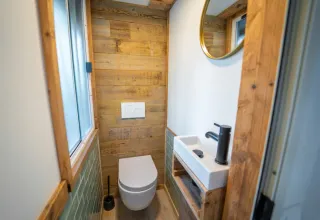 Moderne badkamer met houten wanden, hangend toilet, kleine wastafel en zwarte kraan bij Bohemian Lodge.