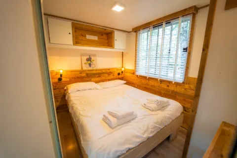 Knusse slaapkamer met houten details en tweepersoonsbed in Bohemian Lodge, Chianti Glamping Resort, Italië.