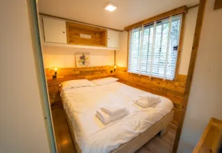 Knusse slaapkamer met houten details en tweepersoonsbed in Bohemian Lodge, Chianti Glamping Resort, Italië.