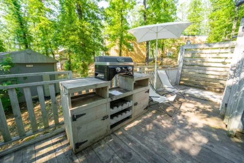 Terras met barbecue, stoelen en parasol bij Bohemian Lodge, Chianti Glamping Resort, omringd door groen.