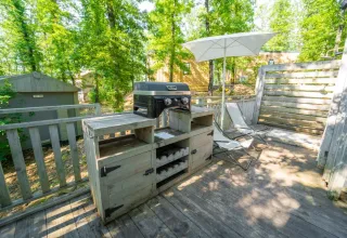 Terras met barbecue, stoelen en parasol bij Bohemian Lodge, Chianti Glamping Resort, omringd door groen.