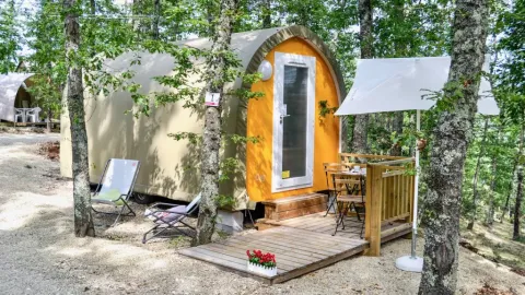 Coco Couple safaritent in het bos met houten terras, stoelen, tafeltje en een witte parasol erbij.