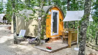 Safari-Zelt Coco Couple im Wald mit Terrasse, Tisch, Stühlen und Sonnenschirm auf einem Campingplatz.