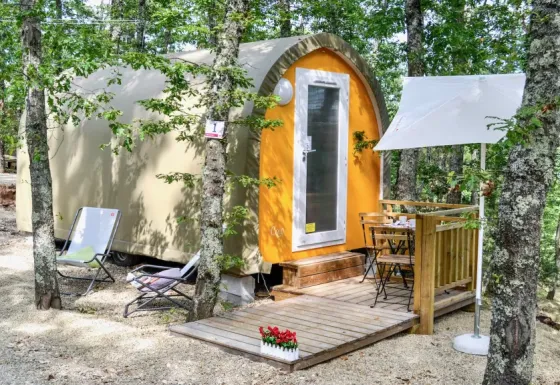 Coco Couple safaritent in het bos met houten terras, stoelen, tafeltje en een witte parasol erbij.