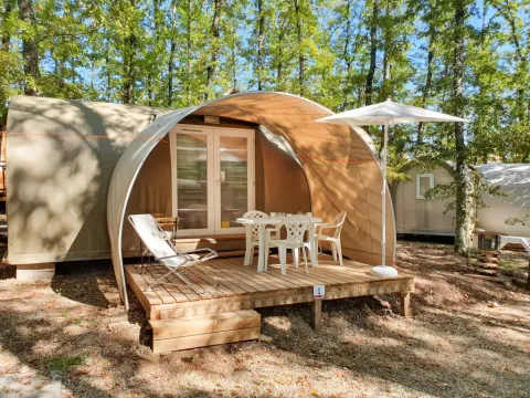 Photo d'une tente safari nommée Coco Suite avec terrasse, chaises, table et parasol en pleine forêt.