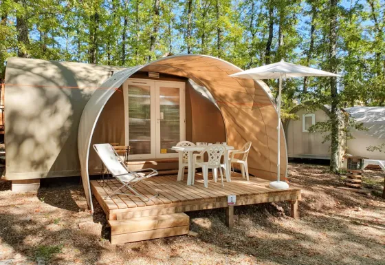 Photo d'une tente safari nommée Coco Suite avec terrasse, chaises, table et parasol en pleine forêt.