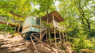 Et charmerende Cottage Classic lodge i skoven, bygget på pæle med træterrasse og omgivet af træer.