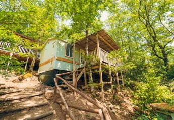 Lodge Cottage Classic su palafitte con terrazza di legno, immerso in una foresta verde lussureggiante.