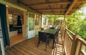 Überdachte Holzterrasse mit Esstisch und Stühlen im Cottage Classic, umgeben von Bäumen im Chianti Glamping Resort.