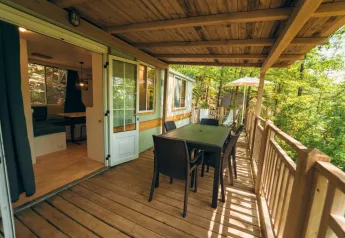 Veranda coperta in legno presso Cottage Classic con tavolo da pranzo, sedie e vista su foresta al Chianti Glamping Resort.