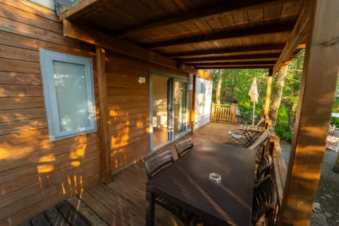 Sonnige Holzterrasse am Cottage Next im Chianti Glamping Resort, Italien, mit Sitzbereich und Waldblick.