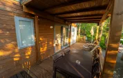 Sonnige Holzterrasse am Cottage Next im Chianti Glamping Resort, Italien, mit Sitzbereich und Waldblick.