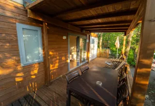 Sonnige Holzterrasse am Cottage Next im Chianti Glamping Resort, Italien, mit Sitzbereich und Waldblick.