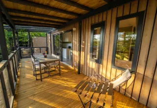 Véranda en bois d’un lodge avec table à manger, chaises et vue sur la nature environnante et les arbres.