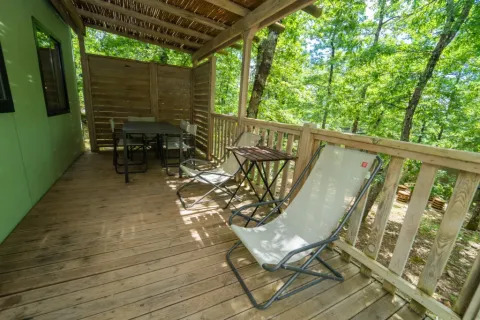 Veranda in legno con sedie e tavolino, immersa tra alberi, al Cottage Next L del Chianti Glamping Resort.