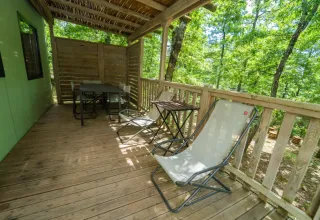 Veranda in legno con sedie e tavolino, immersa tra alberi, al Cottage Next L del Chianti Glamping Resort.