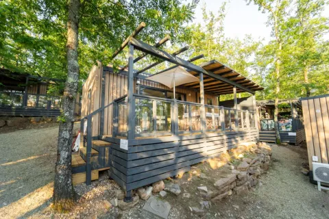 Lodge Cottage Next L Evo dans un cadre boisé, doté d'une terrasse moderne en bois et de rambardes vitrées.