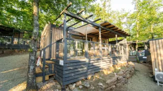 Il Cottage Next L Evo in ambiente boschivo con terrazza in legno moderna e balaustra in vetro.