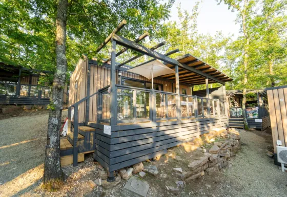 Lodge Cottage Next L Evo dans un cadre boisé, doté d'une terrasse moderne en bois et de rambardes vitrées.