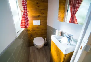 Salle de bains rustique à Cottage Spotty avec murs en bois, rideaux à carreaux rouges, WC et lavabo.