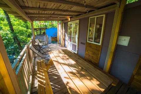 Véranda en bois au Cottage Spotty avec banc, chaises et vue sur la forêt au Chianti Glamping Resort, Italie.