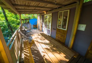 Véranda en bois au Cottage Spotty avec banc, chaises et vue sur la forêt au Chianti Glamping Resort, Italie.