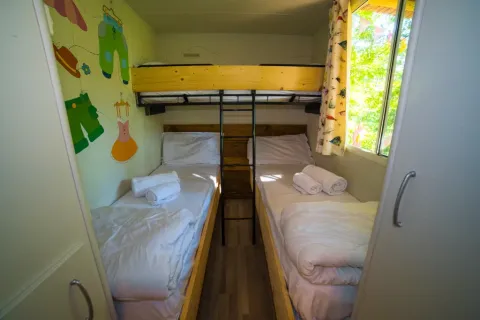 Camera dei bambini con tre letti singoli, decorazioni colorate e finestra al Cottage Spotty nel Chianti Glamping Resort.