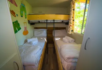 Dormitorio infantil con tres camas individuales, arte colorido en la pared y ventana en Cottage Spotty, Chianti Glamping Resort.