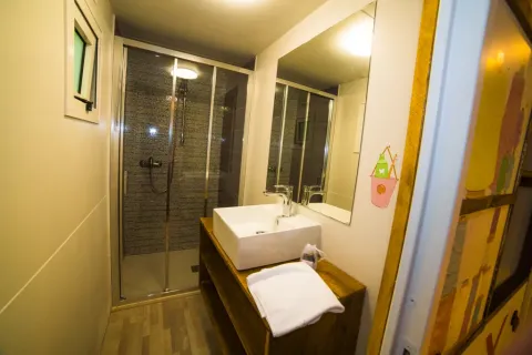 Baño moderno en Cottage Spotty de Chianti Glamping Resort con ducha, lavabo, espejo grande y toalla blanca.