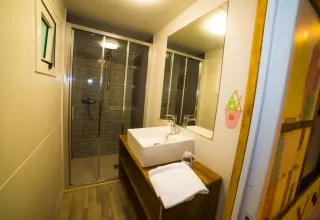 Bagno moderno al Cottage Spotty del Chianti Glamping Resort con doccia, lavabo, grande specchio e asciugamano.