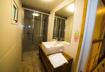 Baño moderno en Cottage Spotty de Chianti Glamping Resort con ducha, lavabo, espejo grande y toalla blanca.