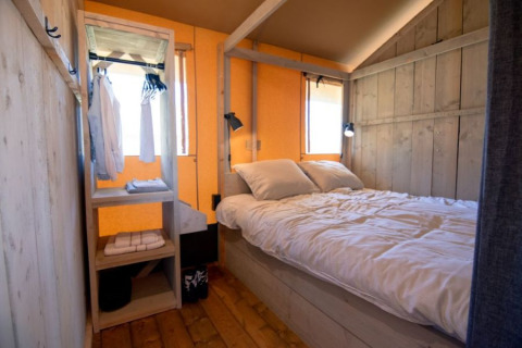 Gezellige slaapkamer met tweepersoonsbed en open kast in De Lodge bij Glamping de Bosweide, Nederland.