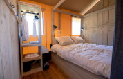 Sfeervolle slaapkamer met tweepersoonsbed en open kast in De Lodge bij Glamping de Bosweide, Nederland.