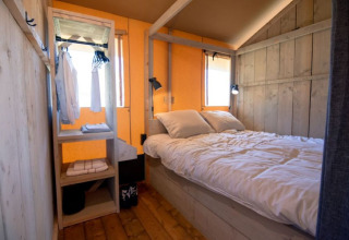 Gezellige slaapkamer met tweepersoonsbed en open kast in De Lodge bij Glamping de Bosweide, Nederland.