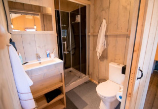 Badkamer met houten afwerking, douche en toilet in De Lodge bij Glamping de Bosweide, Nederland.