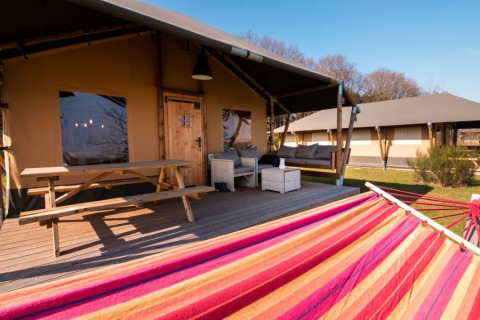 Veranda van 'De Lodge' met picknicktafel, hangmat en zitruimte bij Glamping de Bosweide in Nederland.